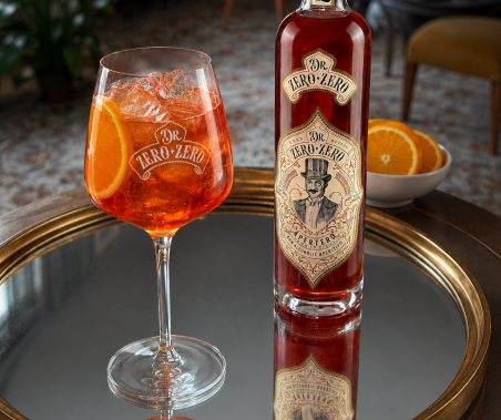 Bottle and glass of Dr. Zero-Zero cocktail on a reflective surface with oranges in the background.