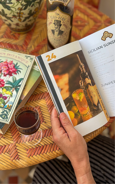 Person holding a book with a drink and bottle on a table